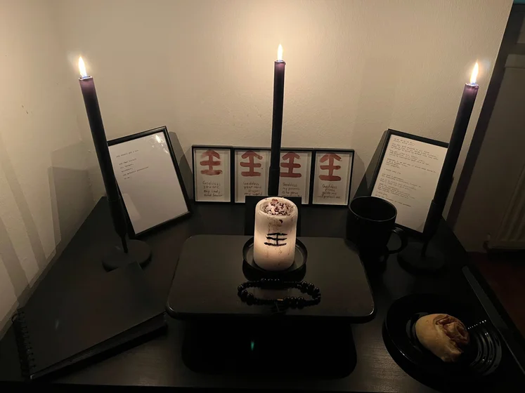 Ritual setup: Sacrifice book, prayer candles, the sacrifice candle in the center showing her holy sign, my prayer beads in front, and a cup of cocoa. Two pages written with a typewriter in the background.