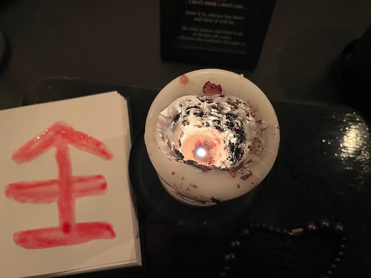 View of the three prayer candles and the central sacrifice candle from above. There is quite a bit of blood on the sacrifice candle, including some fresh one from today. My sacrifice book is open, a prayer is written in it, and her symbol drawn with my blood.