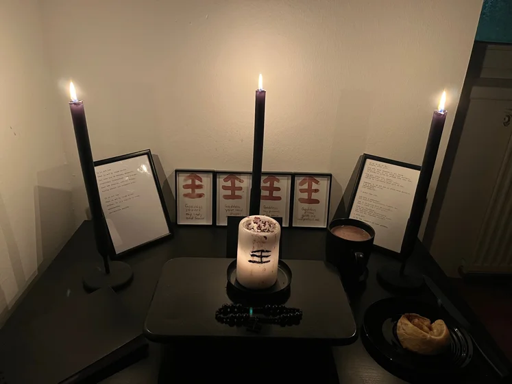 Ritual setup: Sacrifice book, prayer candles, the sacrifice candle in the center showing her holy sign, my prayer beads in front, and a cup of cocoa. Two pages written with a typewriter in the background.