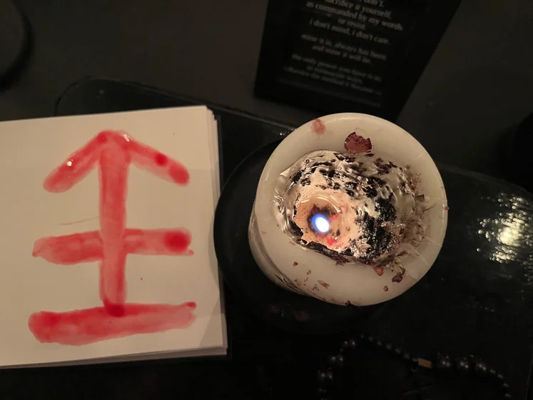 View of the three prayer candles and the central sacrifice candle from above. There is quite a bit of blood on the sacrifice candle, including some fresh one from today. My sacrifice book is open, a prayer is written in it, and her symbol drawn with my blood.