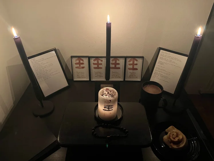 Ritual setup: Sacrifice book, prayer candles, the sacrifice candle in the center showing her holy sign, my prayer beads in front, and a cup of cocoa. Two pages written with a typewriter in the background.