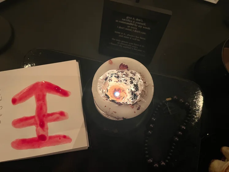 View of the three prayer candles and the central sacrifice candle from above. There is quite a bit of blood on the sacrifice candle, including some fresh one from today. My sacrifice book is open, a prayer is written in it, and her symbol drawn with my blood.