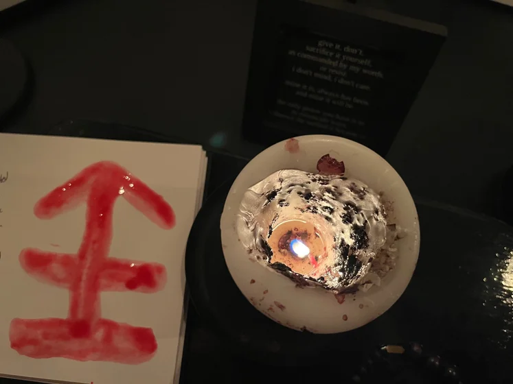View of the three prayer candles and the central sacrifice candle from above. There is quite a bit of blood on the sacrifice candle, including some fresh one from today. My sacrifice book is open, a prayer is written in it, and her symbol drawn with my blood.