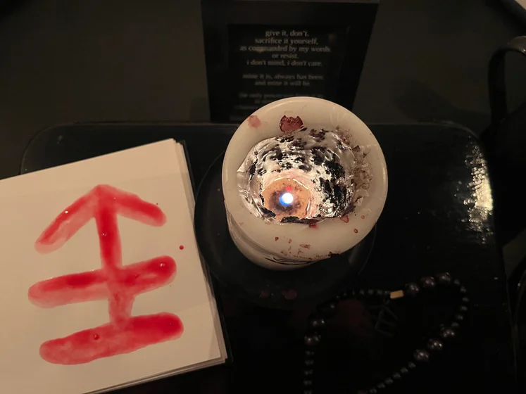 View of the three prayer candles and the central sacrifice candle from above. There is quite a bit of blood on the sacrifice candle, including some fresh one from today. My sacrifice book is open, a prayer is written in it, and her symbol drawn with my blood.