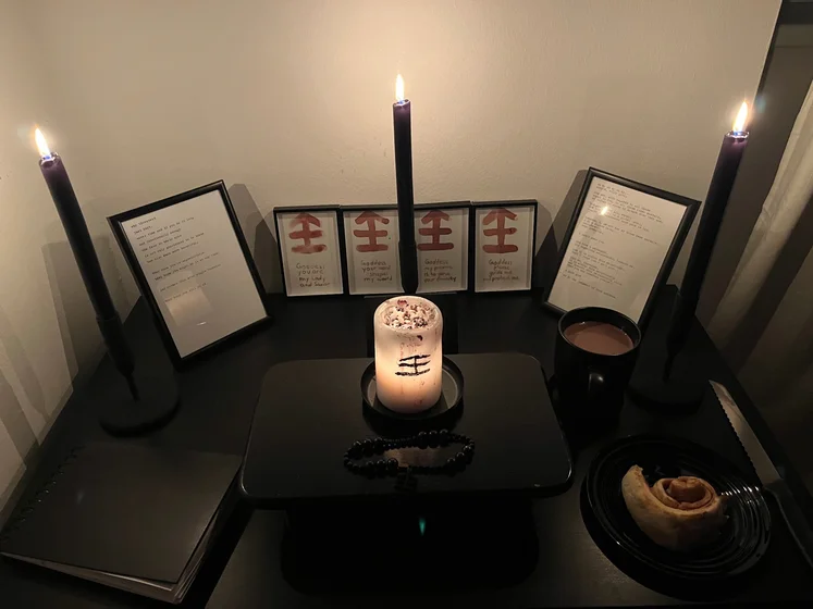 Ritual setup: Sacrifice book, prayer candles, the sacrifice candle in the center showing her holy sign, my prayer beads in front, and a cup of cocoa. Two pages written with a typewriter in the background.
