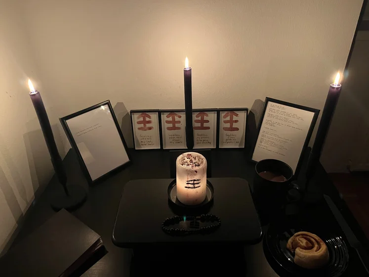 Ritual setup: Sacrifice book, prayer candles, the sacrifice candle in the center showing her holy sign, my prayer beads in front, and a cup of cocoa. Two pages written with a typewriter in the background.