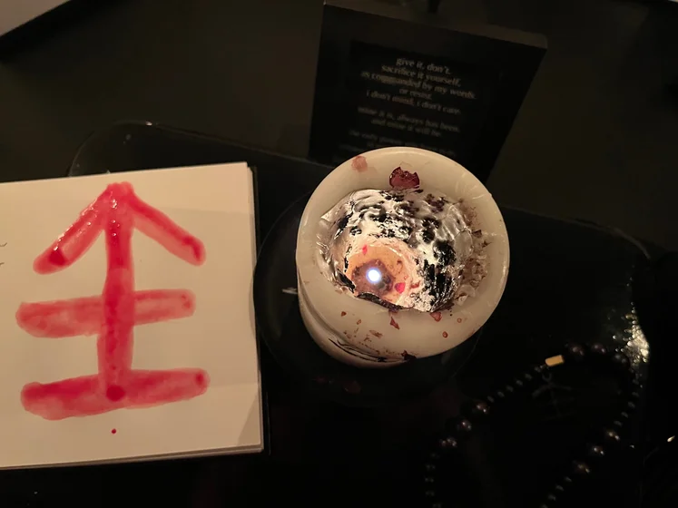 View of the three prayer candles and the central sacrifice candle from above. There is quite a bit of blood on the sacrifice candle, including some fresh one from today. My sacrifice book is open, a prayer is written in it, and her symbol drawn with my blood.