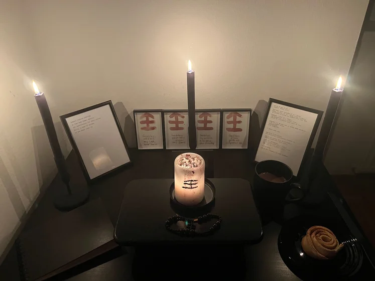 Ritual setup: Sacrifice book, prayer candles, the sacrifice candle in the center showing her holy sign, my prayer beads in front, and a cup of cocoa. Two pages written with a typewriter in the background.