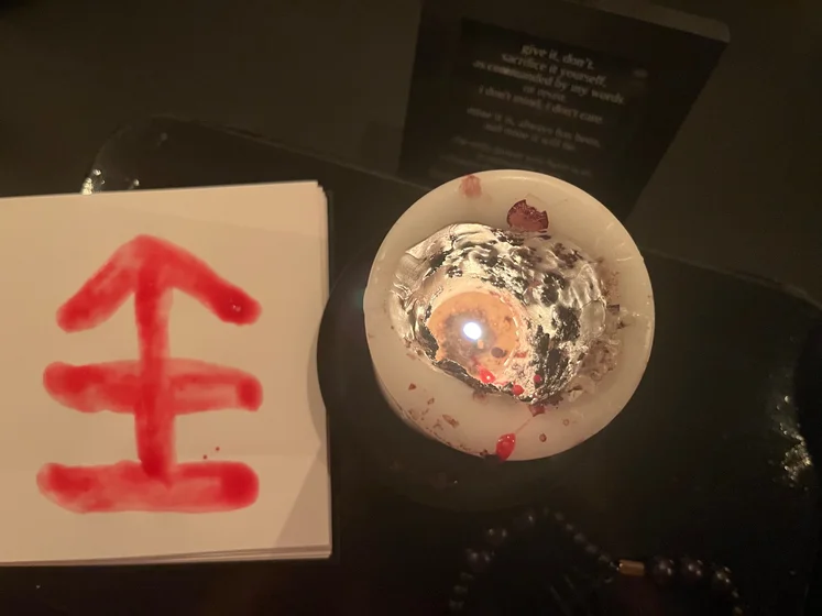 View of the three prayer candles and the central sacrifice candle from above. There is quite a bit of blood on the sacrifice candle, including some fresh one from today. My sacrifice book is open, a prayer is written in it, and her symbol drawn with my blood.