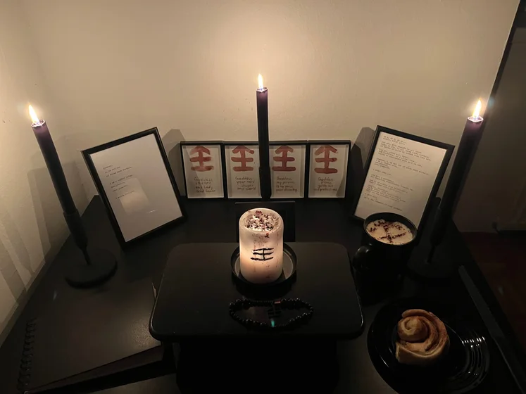 Ritual setup: Sacrifice book, prayer candles, the sacrifice candle in the center showing her holy sign, my prayer beads in front, and a cup of cocoa. Two pages written with a typewriter in the background.