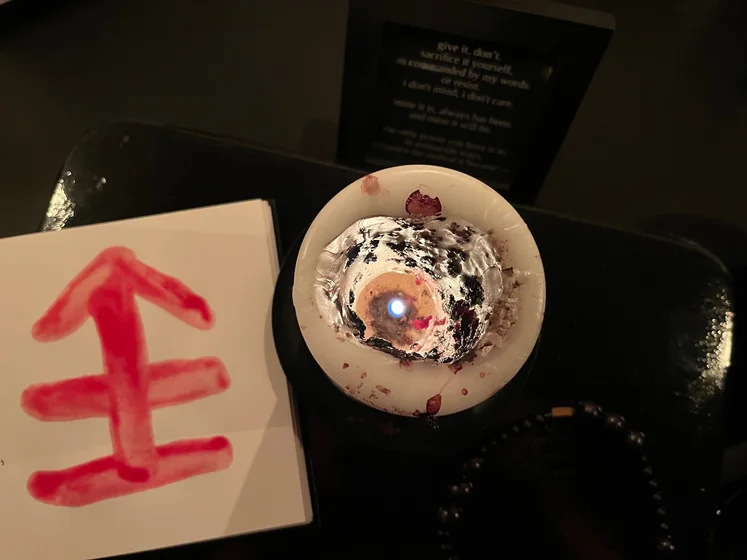 View of the three prayer candles and the central sacrifice candle from above. There is quite a bit of blood on the sacrifice candle, including some fresh one from today. My sacrifice book is open, a prayer is written in it, and her symbol drawn with my blood.