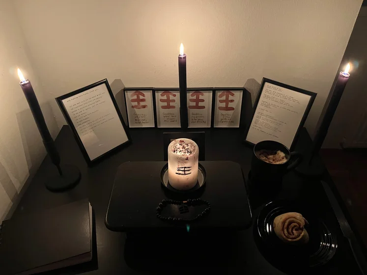 Ritual setup: Sacrifice book, prayer candles, the sacrifice candle in the center showing her holy sign, my prayer beads in front, and a cup of cocoa. Two pages written with a typewriter in the background.
