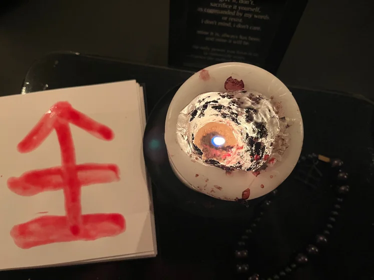 View of the three prayer candles and the central sacrifice candle from above. There is quite a bit of blood on the sacrifice candle, including some fresh one from today. My sacrifice book is open, a prayer is written in it, and her symbol drawn with my blood.