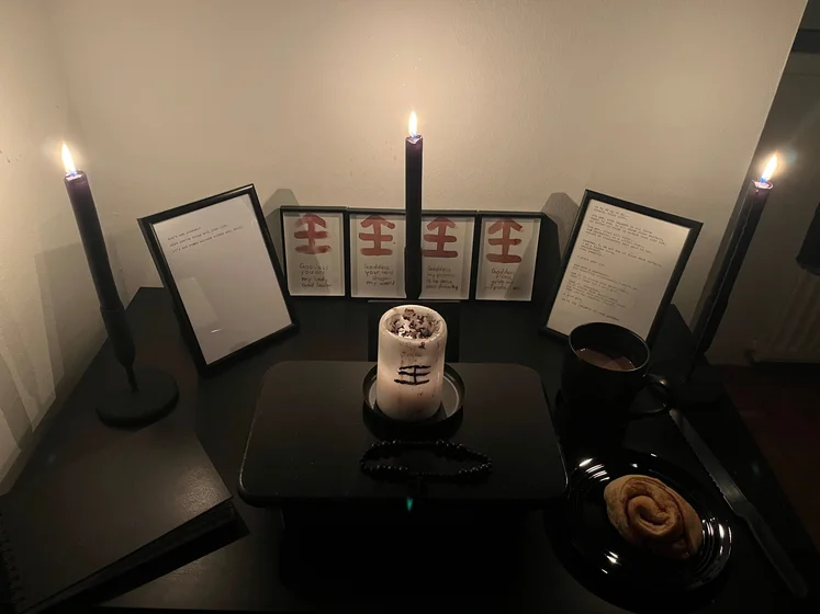 Ritual setup: Sacrifice book, prayer candles, the sacrifice candle in the center showing her holy sign, my prayer beads in front, and a cup of cocoa. Two pages written with a typewriter in the background.