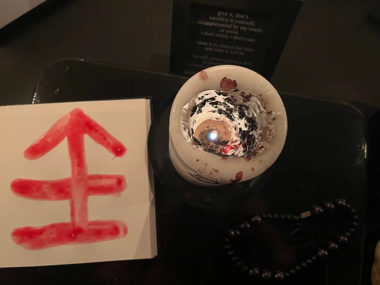 View of the three prayer candles and the central sacrifice candle from above. There is quite a bit of blood on the sacrifice candle, including some fresh one from today. My sacrifice book is open, a prayer is written in it, and her symbol drawn with my blood.