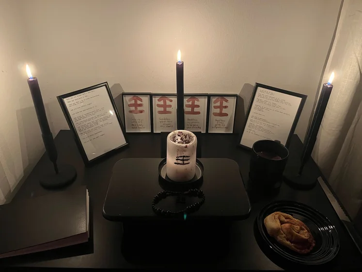 Ritual setup: Sacrifice book, prayer candles, the sacrifice candle in the center showing her holy sign, my prayer beads in front, and a cup of cocoa. Two pages written with a typewriter in the background.