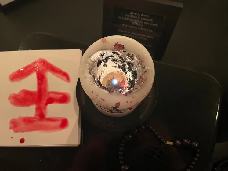 View of the three prayer candles and the central sacrifice candle from above. There is quite a bit of blood on the sacrifice candle, including some fresh one from today. My sacrifice book is open, a prayer is written in it, and her symbol drawn with my blood.