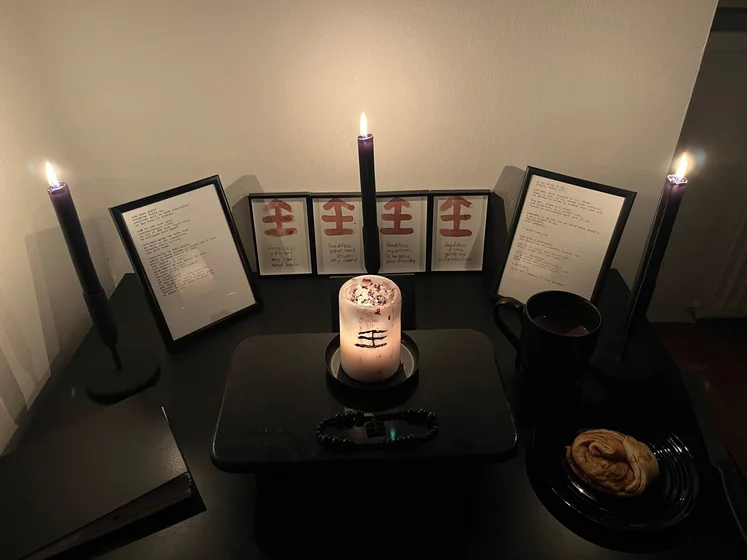 Ritual setup: Sacrifice book, prayer candles, the sacrifice candle in the center showing her holy sign, my prayer beads in front, and a cup of cocoa. Two pages written with a typewriter in the background.