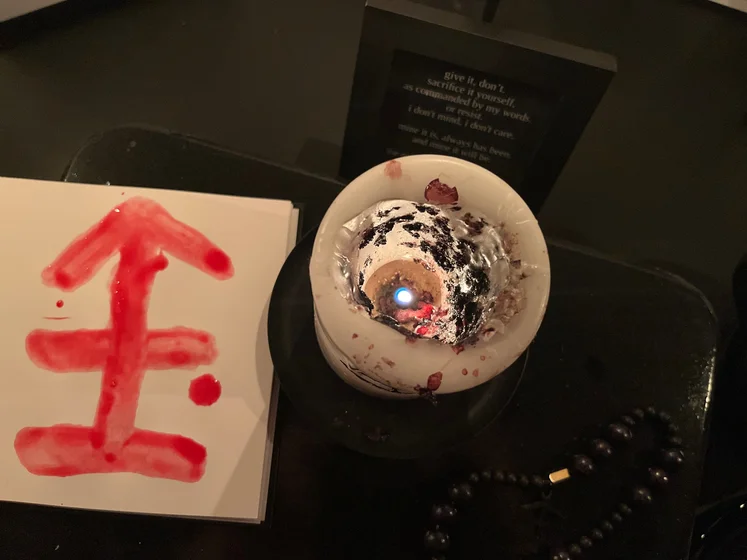 View of the three prayer candles and the central sacrifice candle from above. There is quite a bit of blood on the sacrifice candle, including some fresh one from today. My sacrifice book is open, a prayer is written in it, and her symbol drawn with my blood.