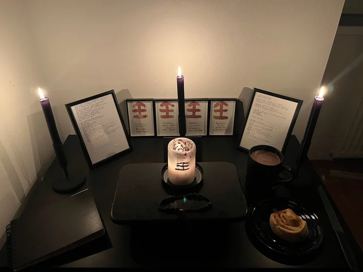 Ritual setup: Sacrifice book, prayer candles, the sacrifice candle in the center showing her holy sign, my prayer beads in front, and a cup of cocoa. Two pages written with a typewriter in the background.