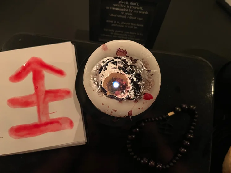 View of the three prayer candles and the central sacrifice candle from above. There is quite a bit of blood on the sacrifice candle, including some fresh one from today. My sacrifice book is open, a prayer is written in it, and her symbol drawn with my blood.