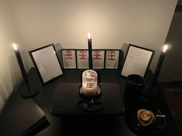 Ritual setup: Sacrifice book, prayer candles, the sacrifice candle in the center showing her holy sign, my prayer beads in front, and a cup of cocoa. Two pages written with a typewriter in the background.