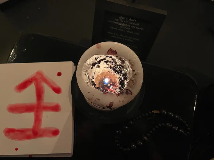 View of the three prayer candles and the central sacrifice candle from above. There is quite a bit of blood on the sacrifice candle, including some fresh one from today. My sacrifice book is open, a prayer is written in it, and her symbol drawn with my blood.
