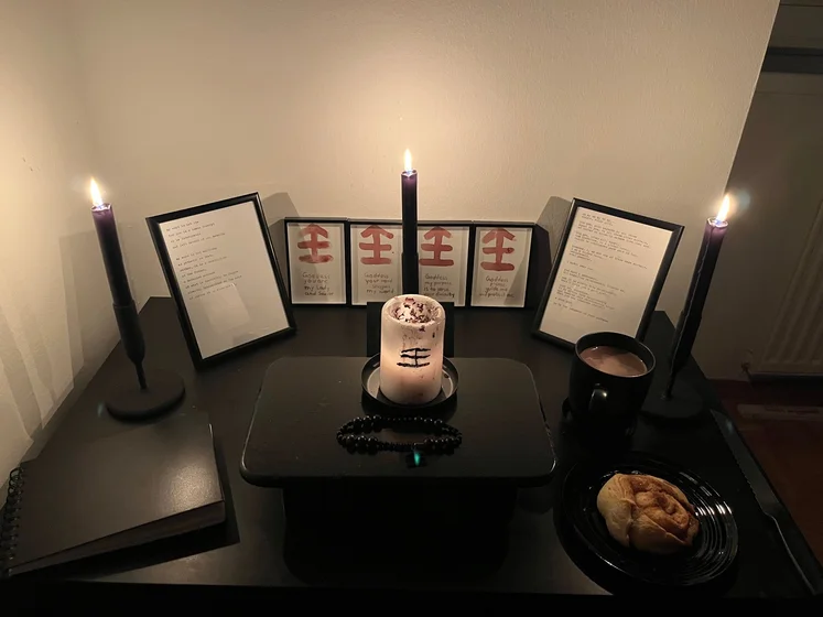Ritual setup: Sacrifice book, prayer candles, the sacrifice candle in the center showing her holy sign, my prayer beads in front, and a cup of cocoa. Two pages written with a typewriter in the background.