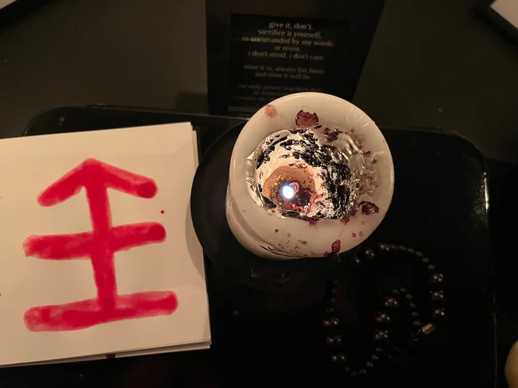 View of the three prayer candles and the central sacrifice candle from above. There is quite a bit of blood on the sacrifice candle, including some fresh one from today. My sacrifice book is open, a prayer is written in it, and her symbol drawn with my blood.