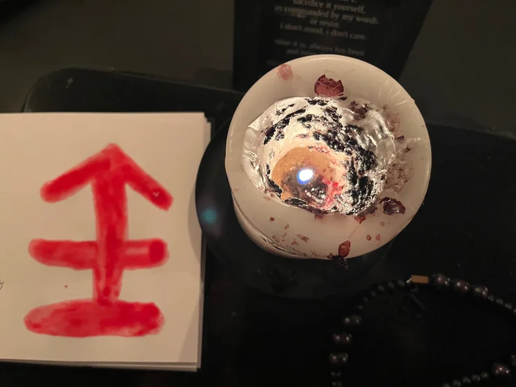Ritual setup: Sacrifice book, prayer candles, the sacrifice candle in the center showing her holy sign, my prayer beads in front, and a cup of cocoa. Two pages written with a typewriter in the background.