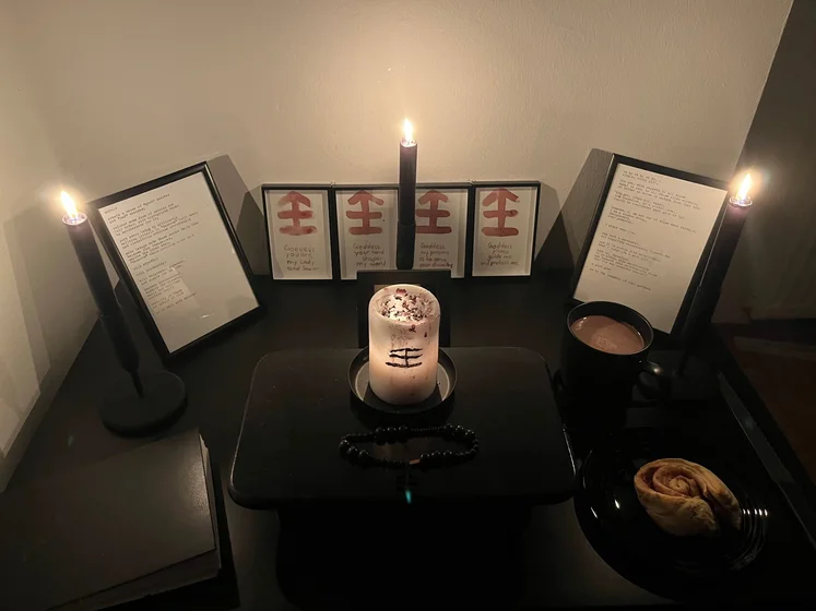Ritual setup: Sacrifice book, prayer candles, the sacrifice candle in the center showing her holy sign, my prayer beads in front, and a cup of cocoa. Two pages written with a typewriter in the background.
