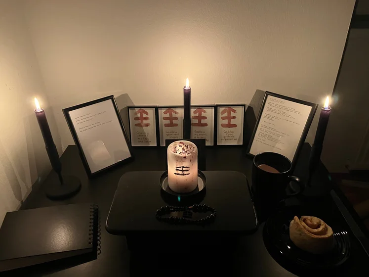 Ritual setup: Sacrifice book, prayer candles, the sacrifice candle in the center showing her holy sign, my prayer beads in front, and a cup of cocoa. Two pages written with a typewriter in the background.