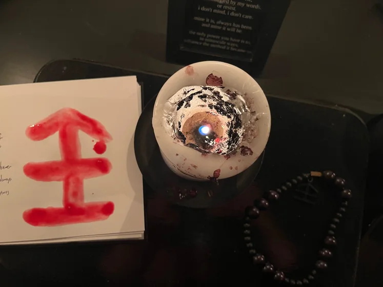 View of the three prayer candles and the central sacrifice candle from above. There is quite a bit of blood on the sacrifice candle, including some fresh one from today. My sacrifice book is open, a prayer is written in it, and her symbol drawn with my blood.