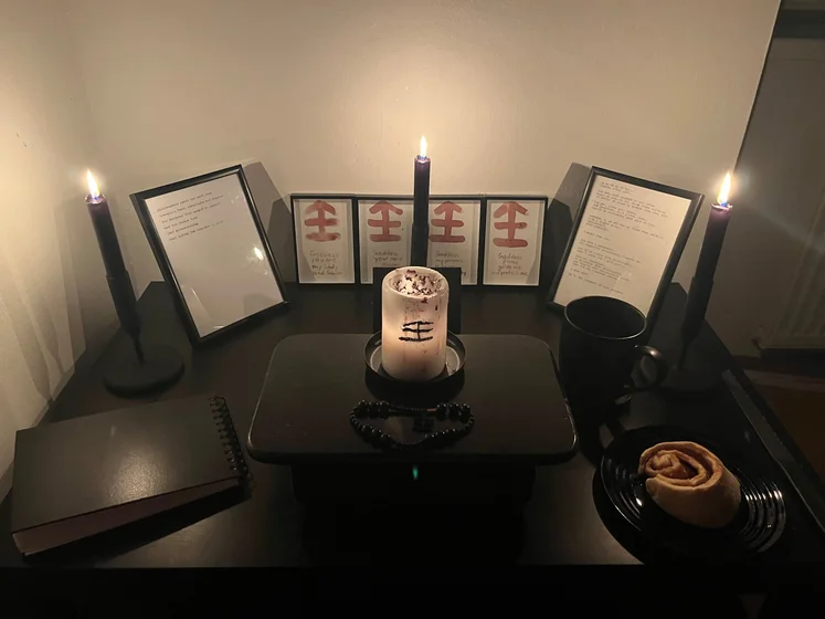 Ritual setup: Sacrifice book, prayer candles, the sacrifice candle in the center showing her holy sign, my prayer beads in front, and a cup of cocoa. Two pages written with a typewriter in the background.