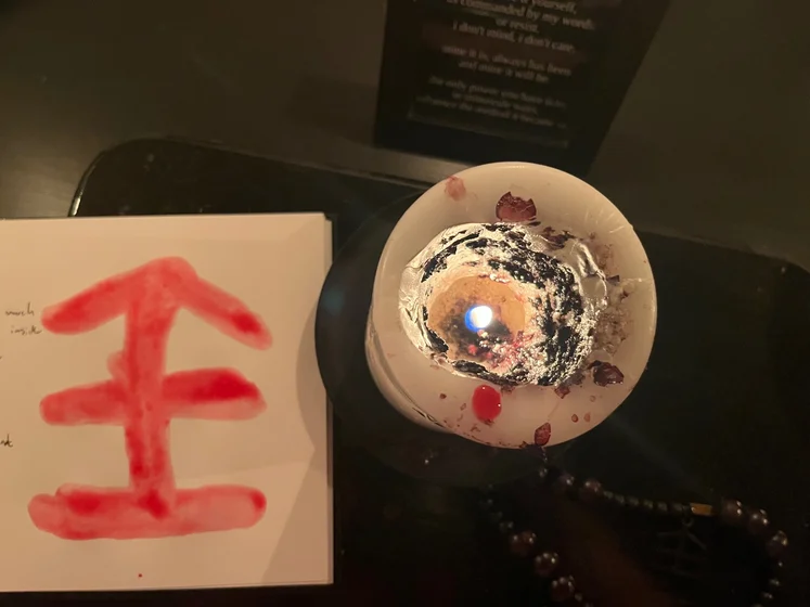 View of the three prayer candles and the central sacrifice candle from above. There is quite a bit of blood on the sacrifice candle, including some fresh one from today. My sacrifice book is open, a prayer is written in it, and her symbol drawn with my blood.