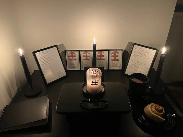 Ritual setup: Sacrifice book, prayer candles, the sacrifice candle in the center showing her holy sign, my prayer beads in front, and a cup of cocoa. Two pages written with a typewriter in the background.