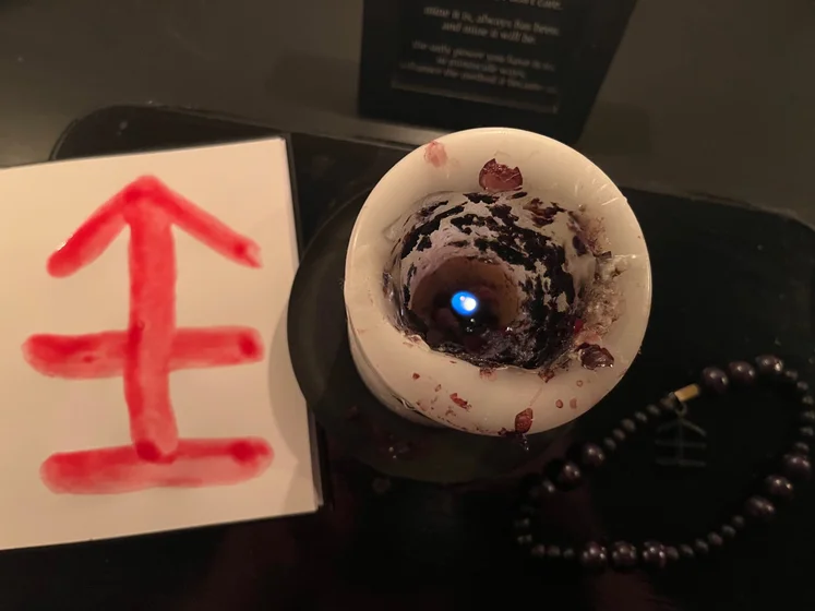 View of the three prayer candles and the central sacrifice candle from above. There is quite a bit of blood on the sacrifice candle, including some fresh one from today. My sacrifice book is open, a prayer is written in it, and her symbol drawn with my blood.