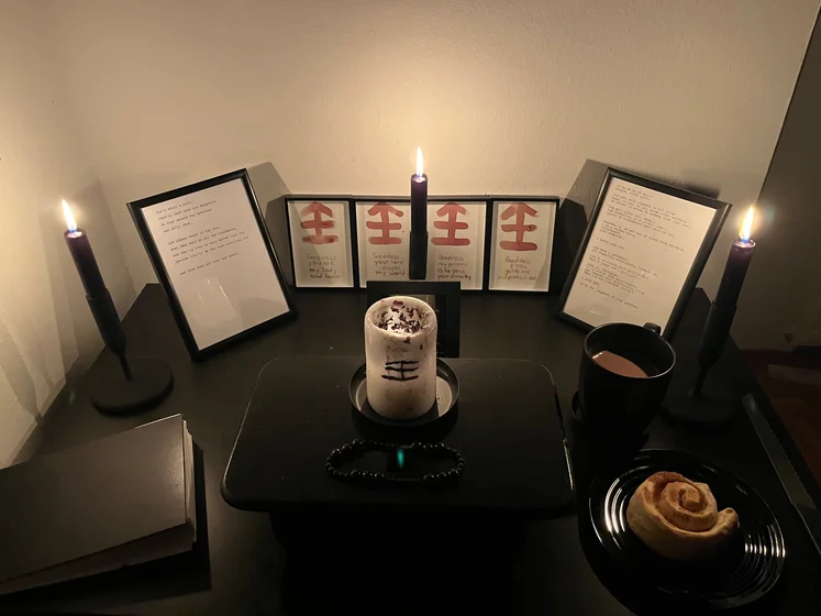 Ritual setup: Sacrifice book, prayer candles, the sacrifice candle in the center showing her holy sign, my prayer beads in front, and a cup of cocoa. Two pages written with a typewriter in the background.