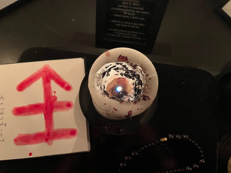 View of the three prayer candles and the central sacrifice candle from above. There is quite a bit of blood on the sacrifice candle, including some fresh one from today. My sacrifice book is open, a prayer is written in it, and her symbol drawn with my blood.